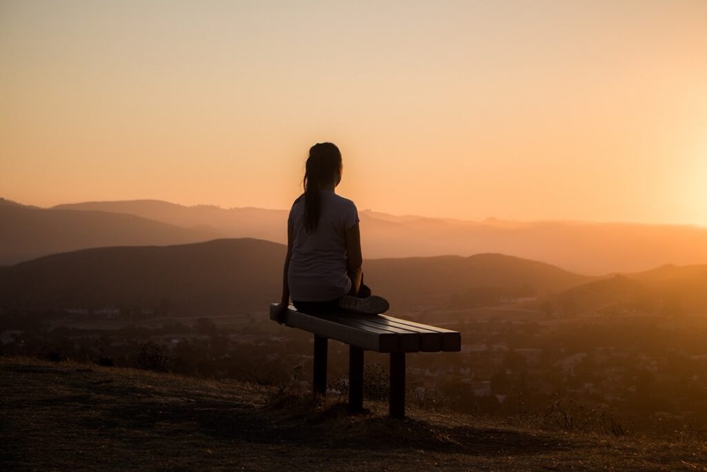 Personne assise sur un banc qui regarde le levée de soleil