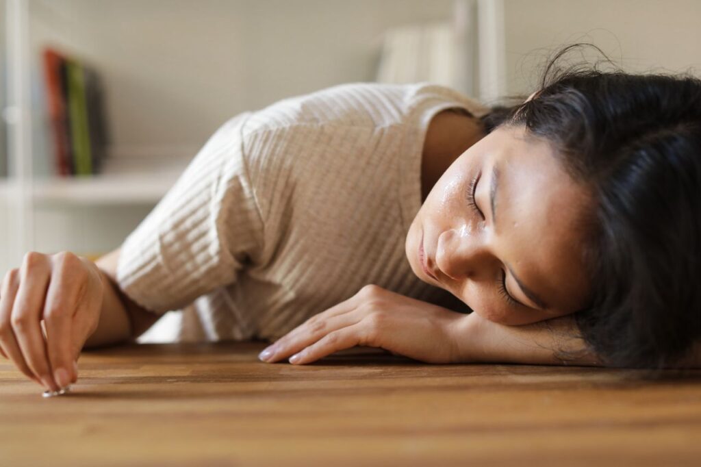 Woman lying on wooden table, appearing emotional, with a small object in hand.