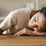 Woman lying on wooden table, appearing emotional, with a small object in hand.
